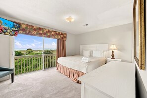 A hotel room with a balcony, a bed with white linens, a bedside table with a lamp, and a view of the ocean. - Oceanfront home with WiFi, central AC, washer/dryer - dogs welcome (Holden Beach)