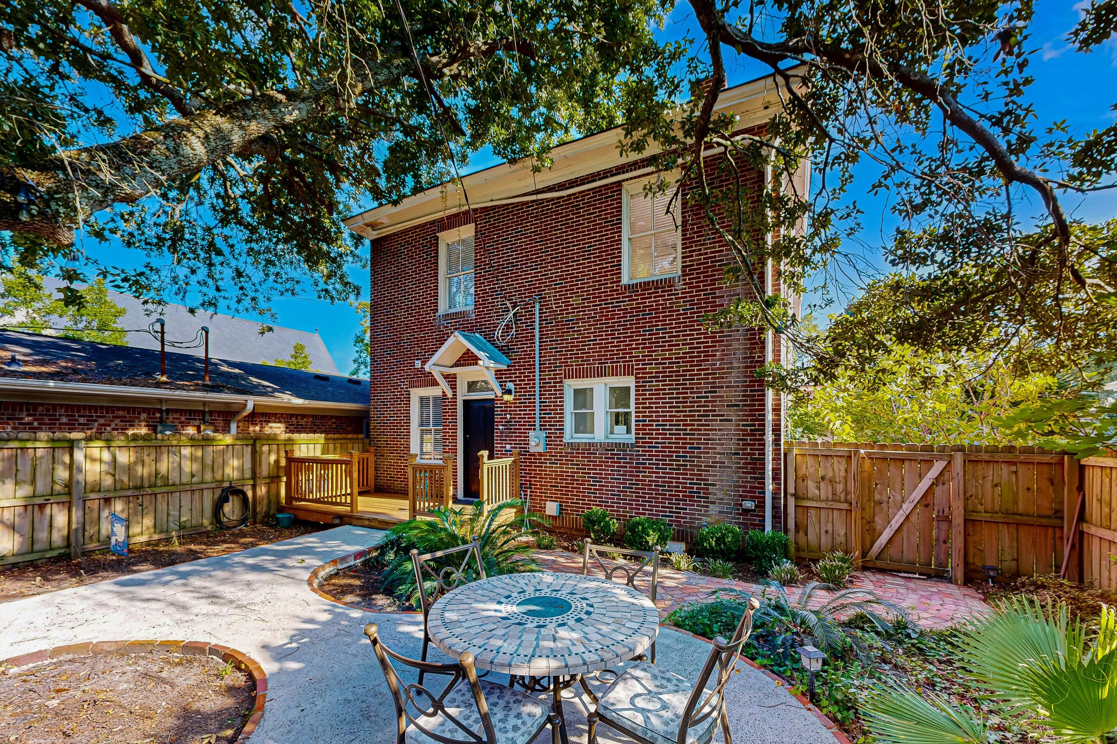 Une maison en briques avec une porte d’entrée, une clôture en bois et une terrasse avec une table et des chaises.