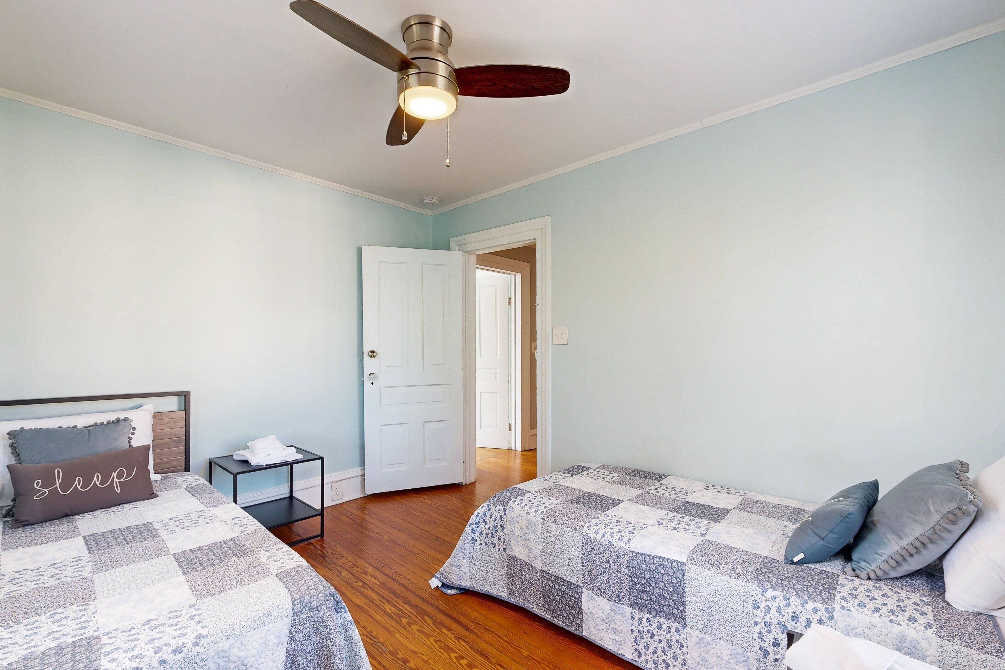 Une chambre avec deux lits, un ventilateur de plafond et une porte donnant sur une autre pièce.