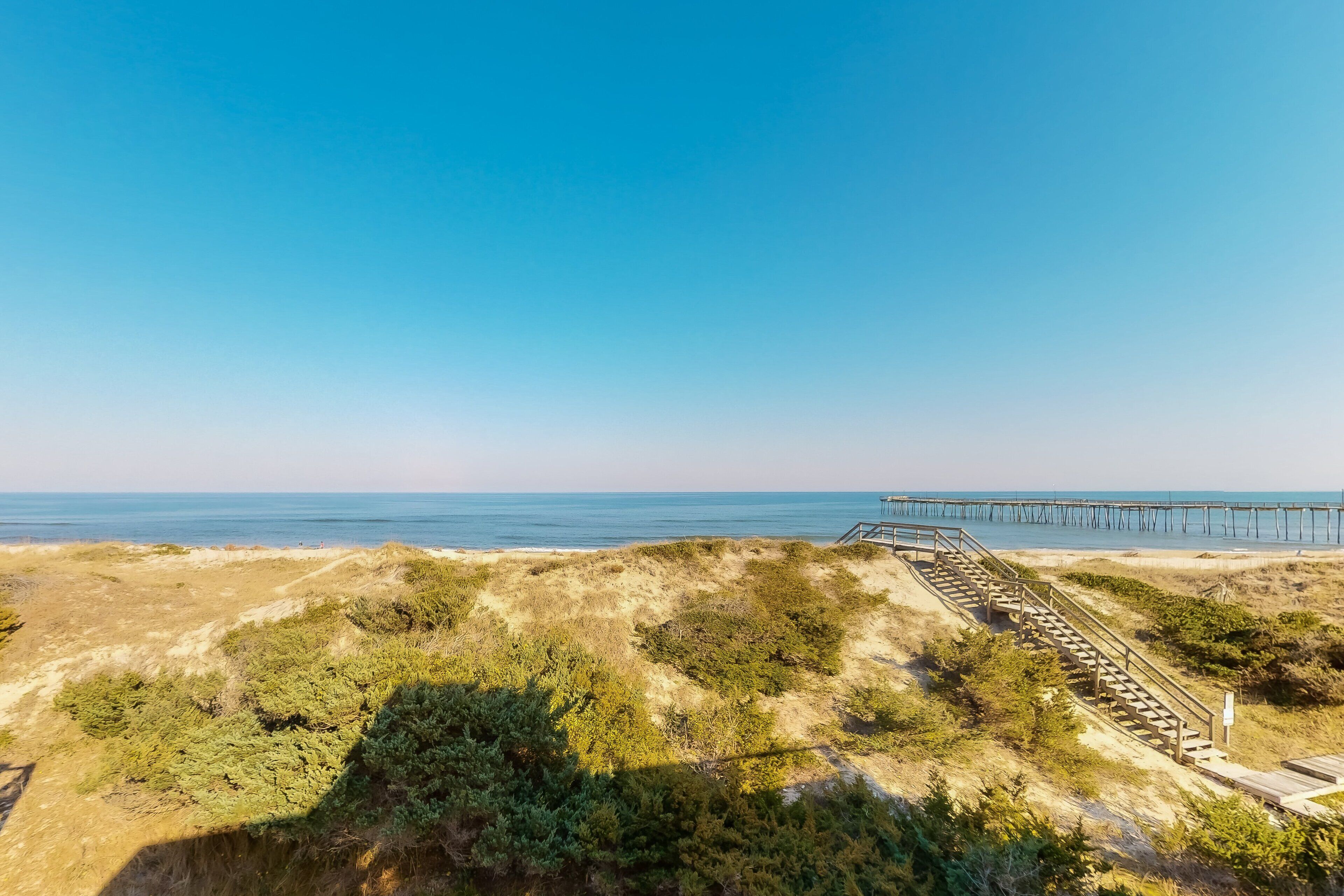 Een kustlandschap met een houten trap die naar een pier leidt, uitstukkend in de zee.