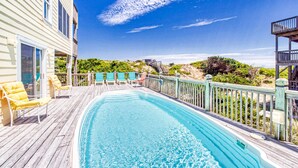Um deck de madeira com piscina, cadeiras amarelas e vista para a praia.