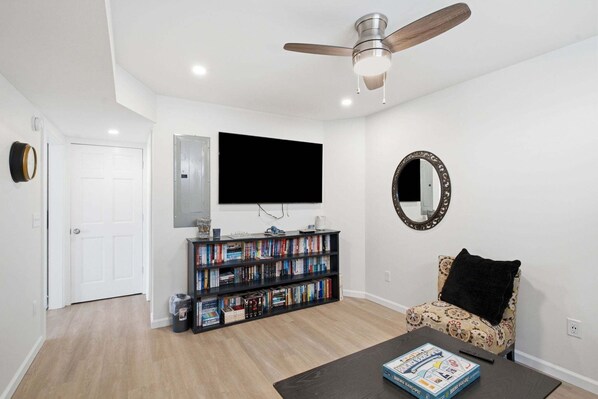 Un salon avec un ventilateur de plafond, une bibliothèque, un téléviseur, un fauteuil et une table basse.