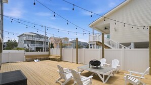 Una terraza con mobiliario exterior, una parrilla y luces colgantes.
