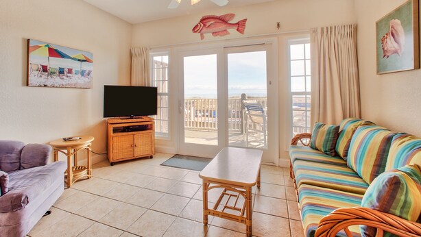 A living room with a sofa, television, and a balcony with a view.