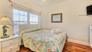 A bedroom with a bed, a nightstand, a lamp, a framed picture, and a ceiling fan.