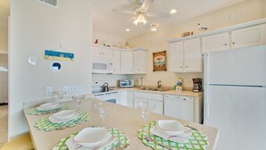 A modern kitchen with white cabinets, a central island with green placemats, and a ceiling fan.