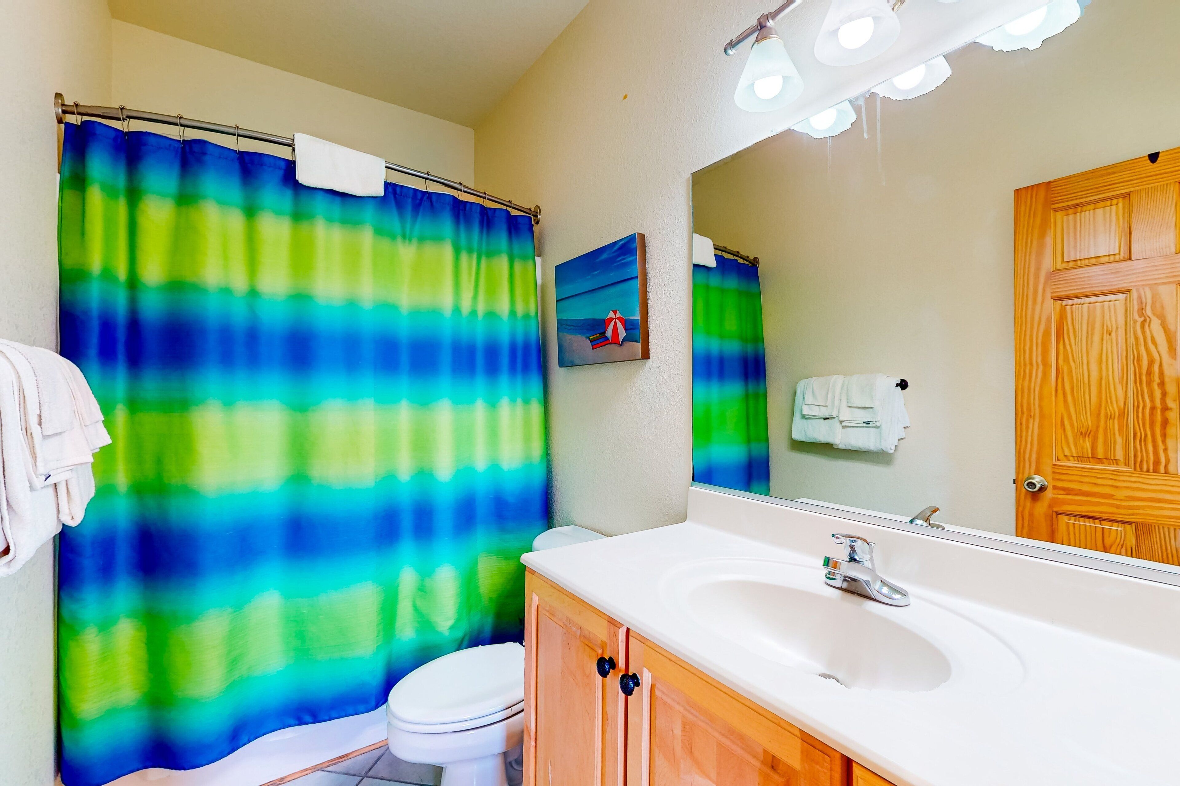 A bathroom with a shower curtain, a toilet, a sink, and a mirror.