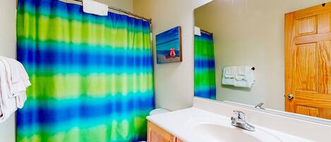 A bathroom with a shower curtain, a toilet, a sink, and a mirror.