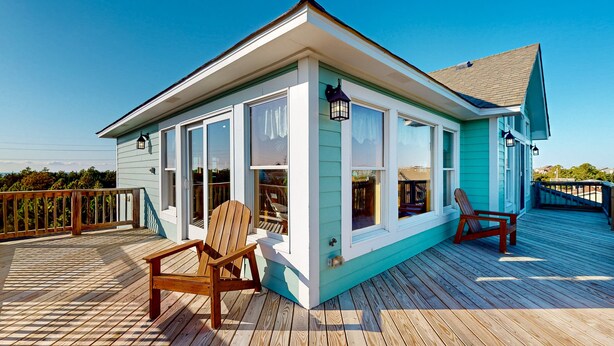 Una casa con una terraza, dos sillas de madera y un ventanal.