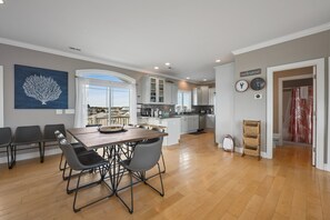 Una cocina moderna con armarios blancos, un comedor con mesa y sillas de madera, y vistas a través de un ventanal.