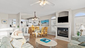 A spacious living room with a fireplace, dining area, and kitchen in the background. - Turtle's Watch: Canal-front dog-friendly home near beach, canal view, & dock (Holden Beach)