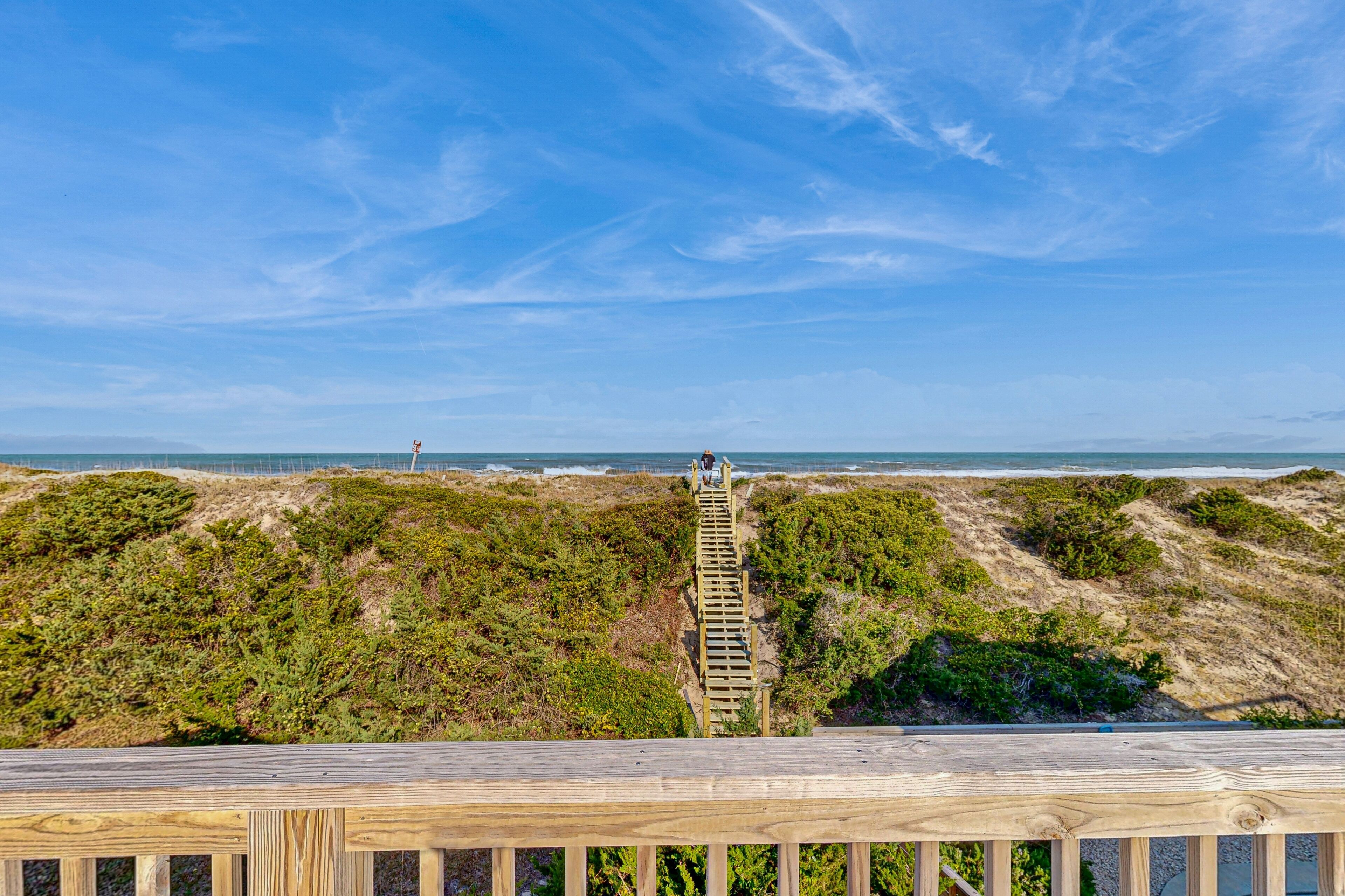 A wooden staircase leading to a beach with a lighthouse in the distance.