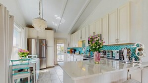 Eine moderne Küche mit weißen Schränken, einem Edelstahlkühlschrank, einer zentralen Kochinsel und einer dekorativen Spritzschutzwand.