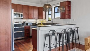 A modern kitchen with wooden cabinets, stainless steel appliances, a central island with bar stools, and pendant lighting. - Perfect Retreat with Private Hot Tub, Panoramic Views, Full Kitchen pet-friendly (Buxton)