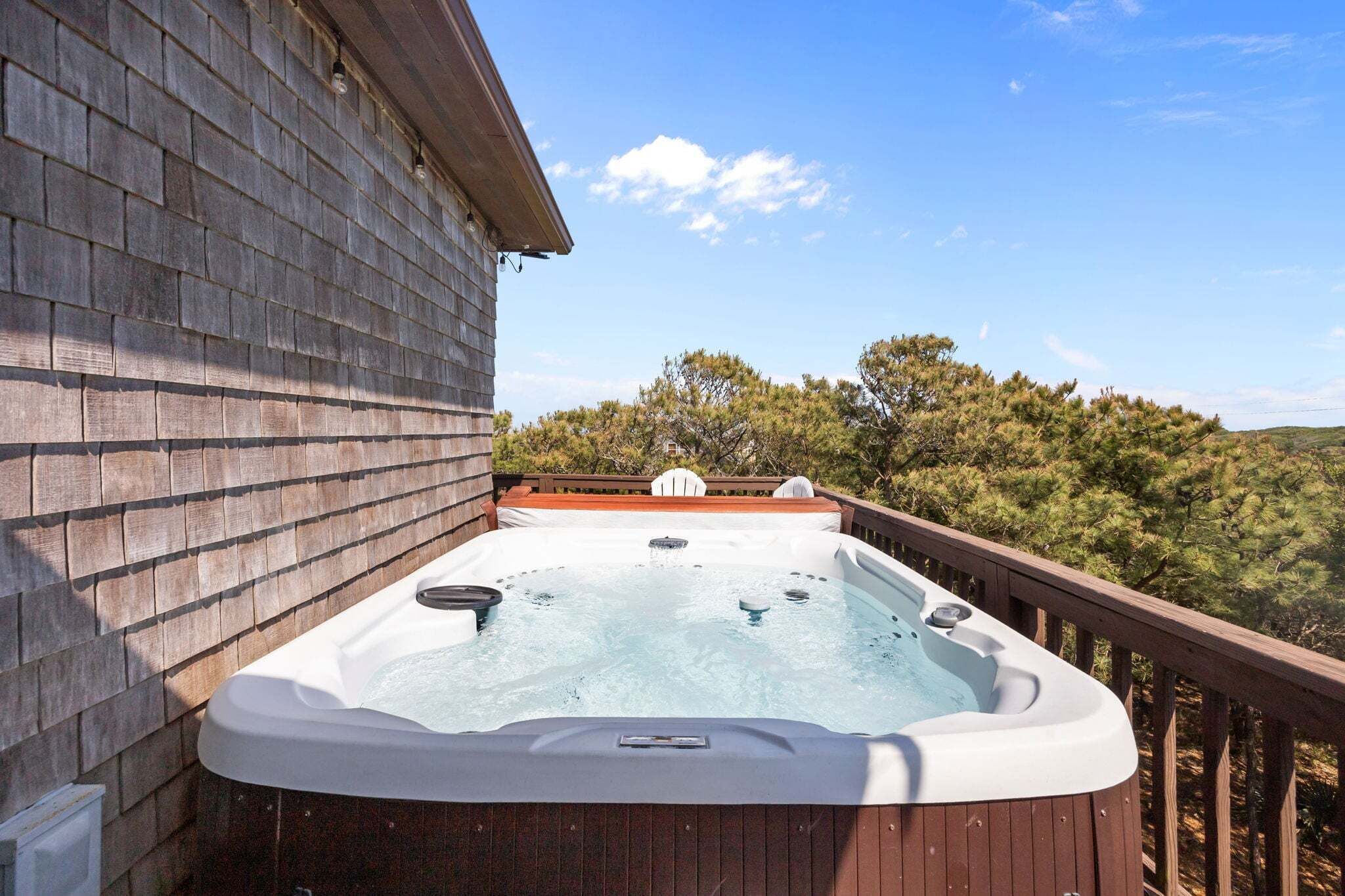 A hot tub on a wooden deck with a view of trees and hills.