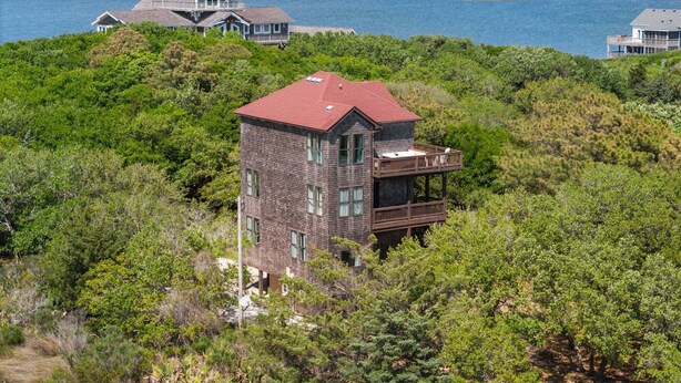 A multi-story building with a red roof, surrounded by dense greenery and overlooking a body of water. - Perfect Retreat with Private Hot Tub, Panoramic Views, Full Kitchen pet-friendly (Buxton)
