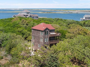 A multi-story building with a red roof, surrounded by dense greenery and overlooking a body of water.
