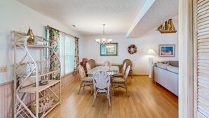 A dining area with a table and chairs, a chandelier, and a wicker shelf with baskets. - Coastal home with large deck, close to beach and local attractions (Holden Beach)