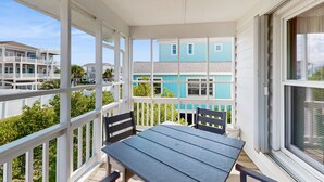 A covered balcony with a table and chairs, overlooking a residential area with houses. - Coastal home with large deck, close to beach and local attractions (Holden Beach)