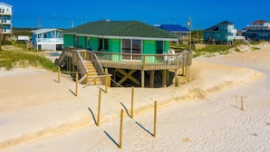 A beach house with a green roof, wooden deck, and a staircase leading to the entrance. - Dog-friendly beachfront home with beach access, ocean views (North Topsail Beach)