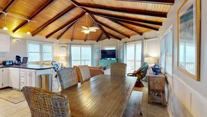 A spacious kitchen with a wooden ceiling, a dining area with wicker chairs, and a large TV in the background. - Dog-friendly beachfront home with beach access, ocean views (North Topsail Beach)