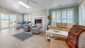 A spacious living room with a ceiling fan, a fireplace, and a large window with blinds. - Dog-friendly marsh view home with large deck, close to beach access (Holden Beach)