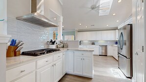 A modern kitchen with white cabinetry, a stainless steel range hood, and a built-in oven. - Dog-friendly marsh view home with large deck, close to beach access (Holden Beach)