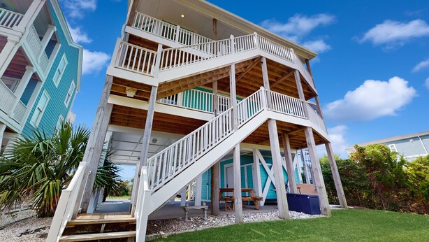 Ein mehrstöckiges Holzhaus mit weißer Treppe, einem Balkon und einer Veranda.