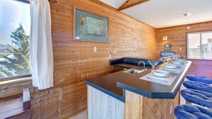 A wooden interior with a kitchen island, bar stools, and a window with a curtain. - Brigadune 143: Dog Friendly, Ocean view, 3 lots from beach (Avon)