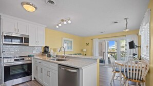 A kitchen with white cabinets, a microwave, an oven, and a dishwasher. There is a dining area with a table and chairs.
