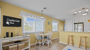 A kitchen with a dining area, a TV displaying 'Carolina Coast Retreats,' and a refrigerator.