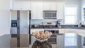A modern kitchen with white cabinets, a stainless steel refrigerator, a microwave, and a granite countertop. - Elegant beachfront escape with private boardwalk, free WiFi, & furnished balcony (Carolina Beach)