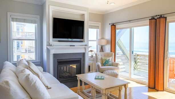 A living room with a fireplace, a television mounted above it, a sofa, a coffee table, and a chair. - Elegant beachfront escape with private boardwalk, free WiFi, & furnished balcony (Carolina Beach)