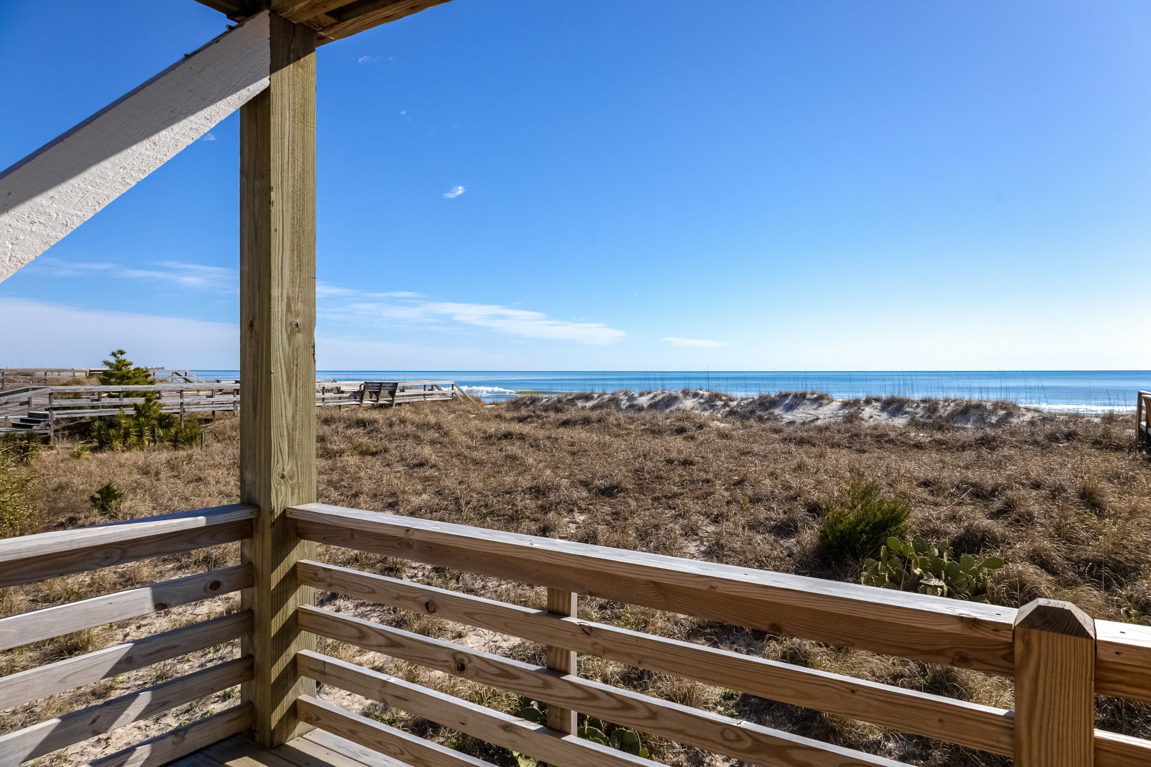 A wooden deck overlooking a beach with dunes and a clear sky.
