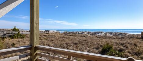 A wooden deck overlooking a beach with dunes and a clear sky.