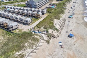 A coastal hotel with multiple-story buildings, a beach area with umbrellas, and a swimming pool.