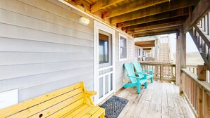 Une terrasse en bois avec un banc et des fauteuils Adirondack, un espace couvert avec un escalier menant à un niveau supérieur.