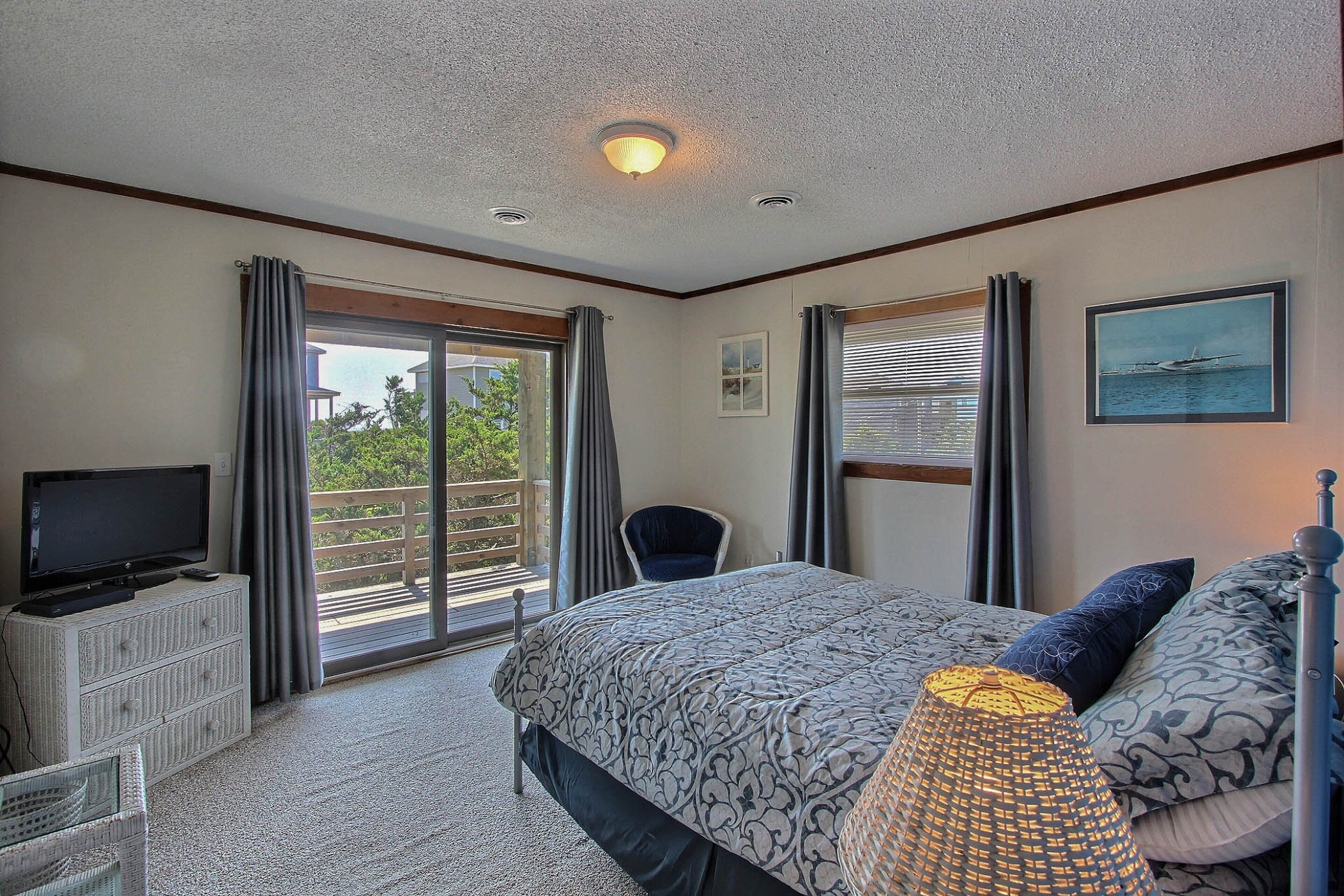 A bedroom with a bed, a television on a dresser, a chair, and a balcony with curtains.