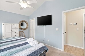 Ein Schlafzimmer mit Bett, Kommode, Schminktisch, Spiegel, Fernseher und Deckenventilator.