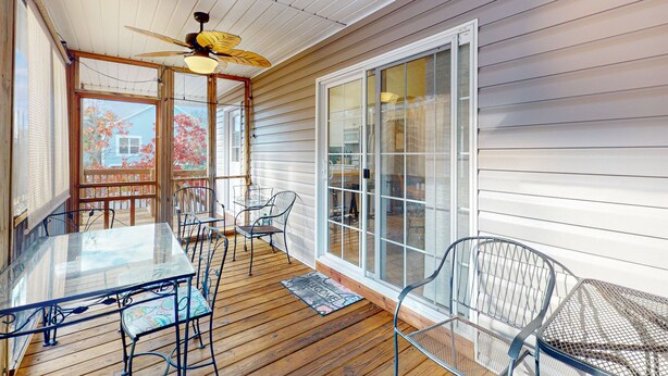 Eine überdachte Terrasse mit Glastisch und Metallstühlen, Holzboden und Deckenventilator.