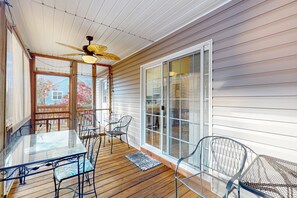 A covered patio with a glass table and metal chairs, wooden flooring, and a ceiling fan. - Seas the Day | Screened Porch & Bikes | Walk to Beach & Intracoastal Waterway (Oak Island)