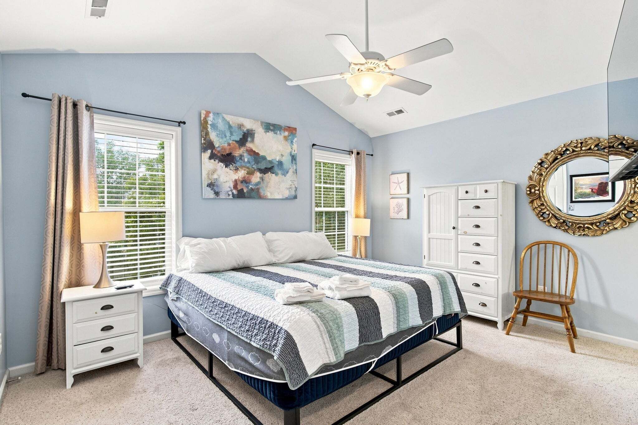 A bedroom with a bed, a nightstand, a dresser, a chair, a ceiling fan, and artwork on the walls.