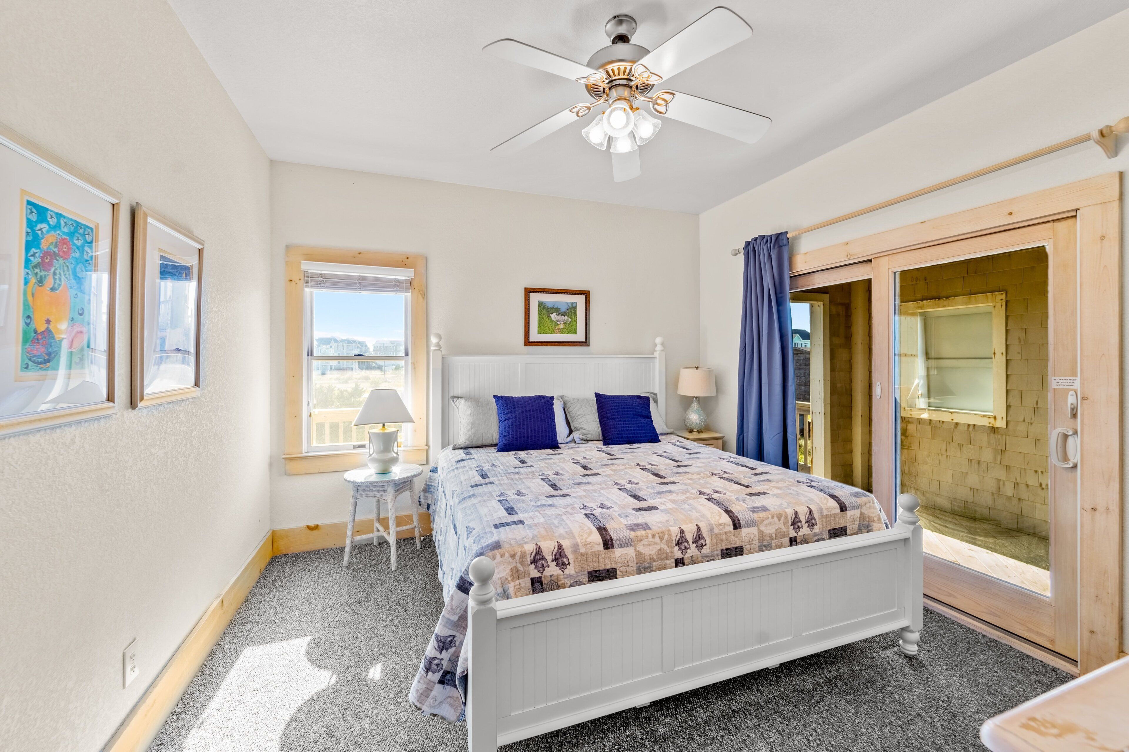 Une chambre à coucher comprenant un lit, un ventilateur de plafond, une fenêtre et une porte donnant sur un espace extérieur.
