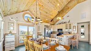A spacious kitchen with wooden ceiling and cabinetry, a dining area with a wooden table and chairs, and a view through the glass doors. - Sprawling & luxe home with pool, hot tub, balconies, grill, game room, & AC (Hatteras)