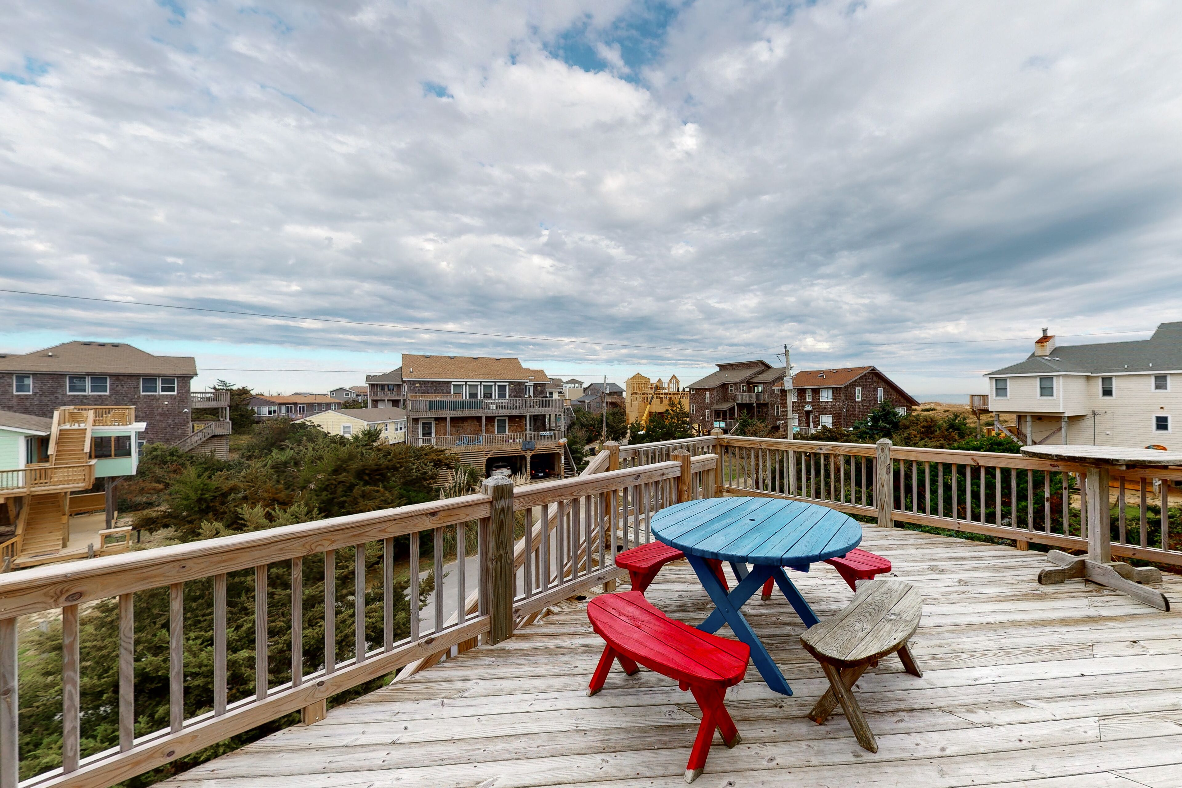 Une terrasse en bois, dotée de tables de pique-nique et d’une rambarde, qui offre une vue sur un quartier résidentiel.