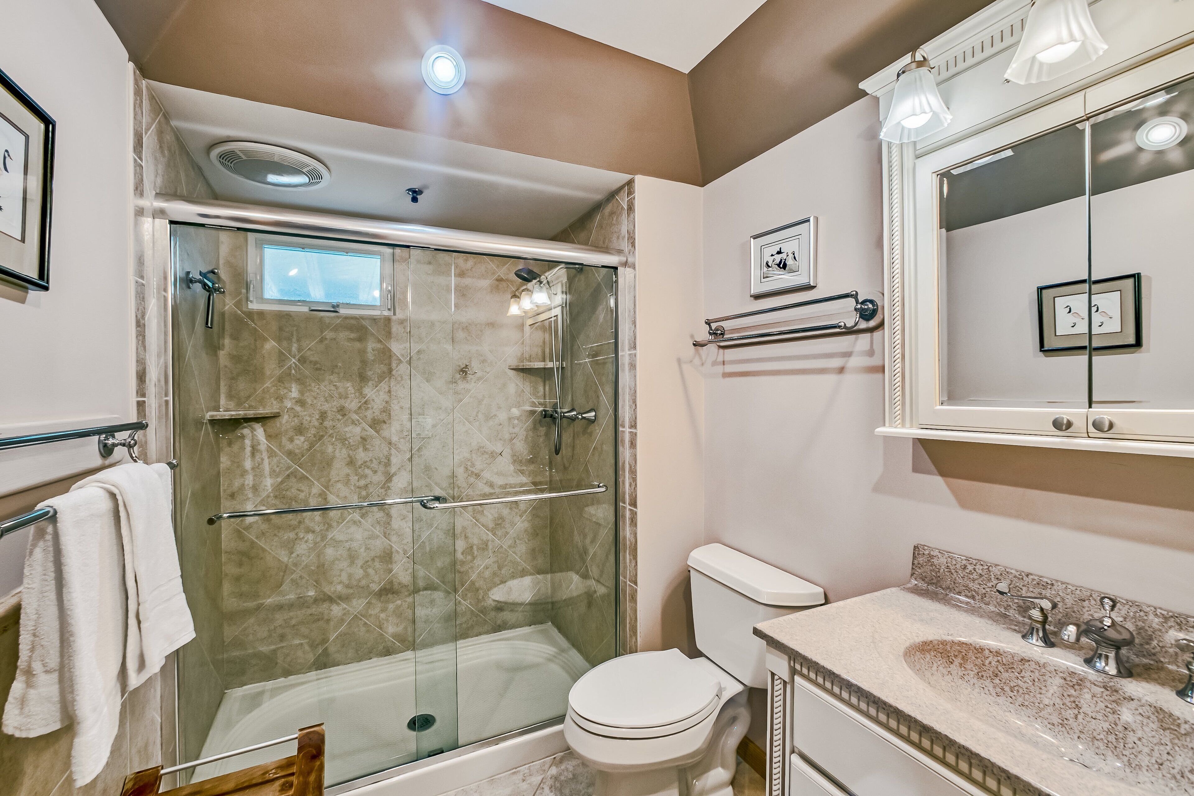 Een moderne badkamer met een douchecabine van glas, een toilet en een wastafel met spiegel erboven.