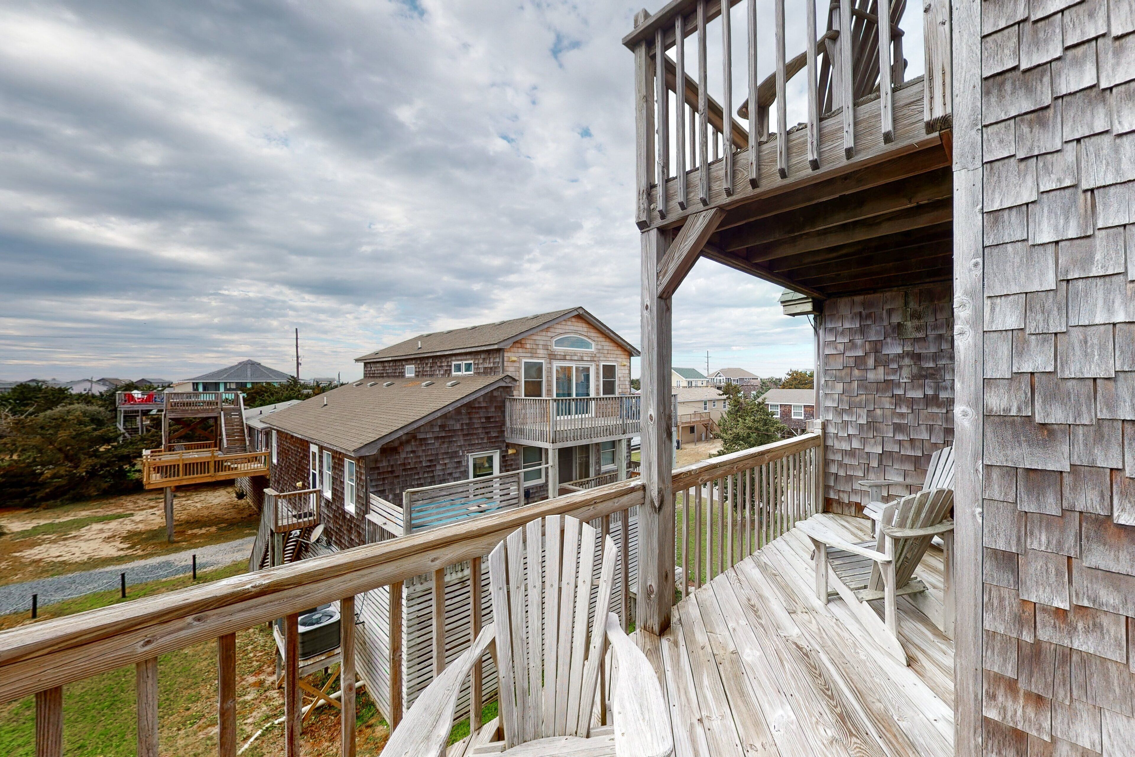 A wooden deck with a railing, a wooden house with a balcony, and a view of other houses in the background.