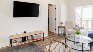 Ein modernes Wohnzimmer mit einem Flachbildfernseher, einer hölzernen Bank, einem Glastisch und einer Couch.