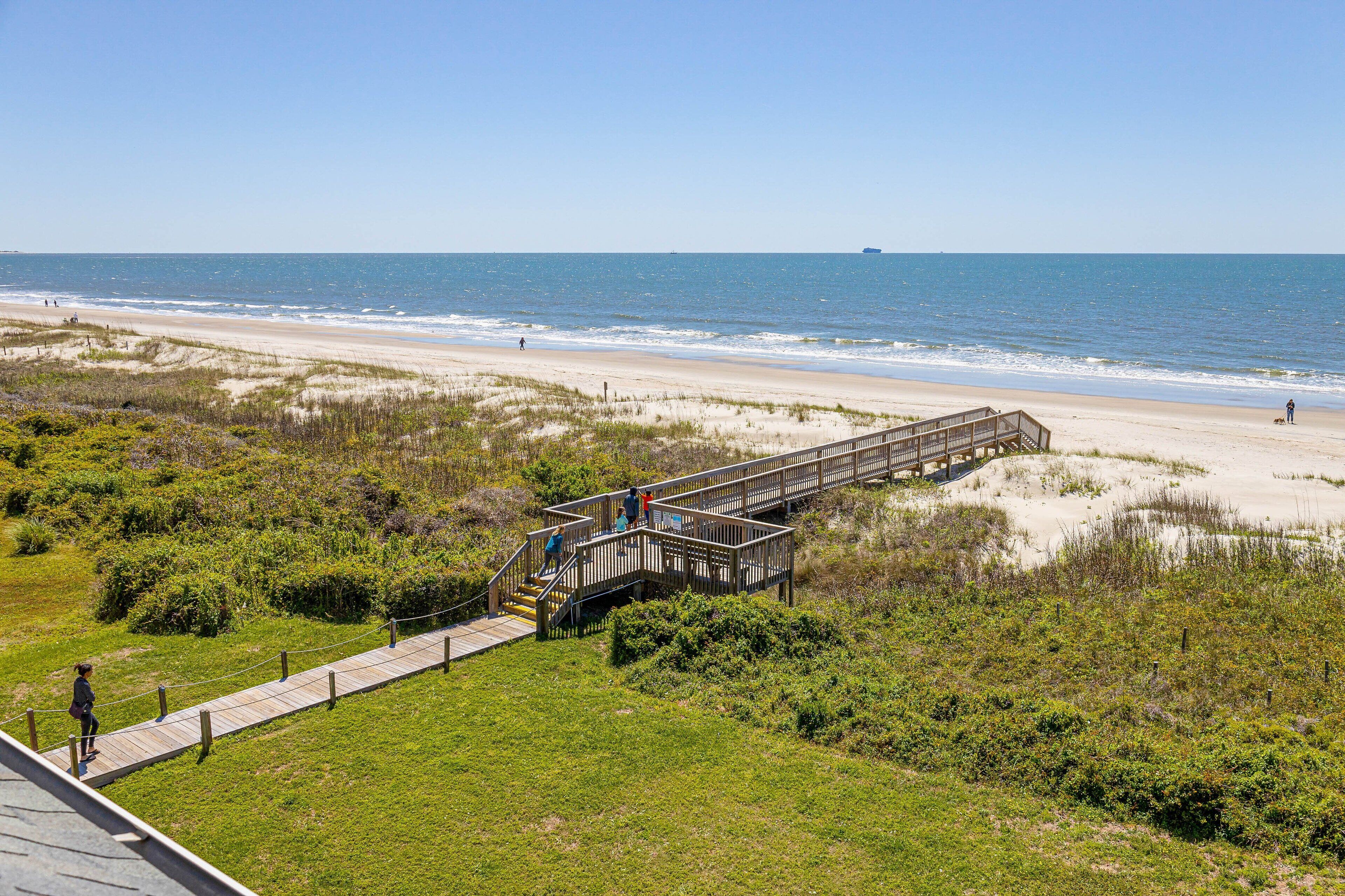 A wooden boardwalk leading to a beach with a clear view of the ocean and distant ship.