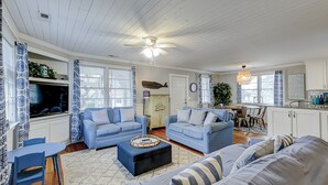 A spacious living room with two blue sofas, a coffee table, and a dining area with a table and chairs. - My Three Buoys: Cozy stay close to everything with backyard, bikes, grill, & washer/dryer (Oak Island)